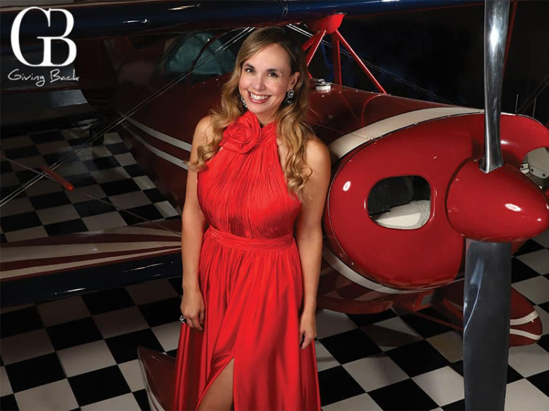 Danitza Villanuela of GB Magazine wearing a red gown in front of red small plane